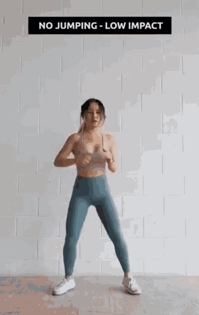 a woman is standing in front of a white brick wall and doing a workout .