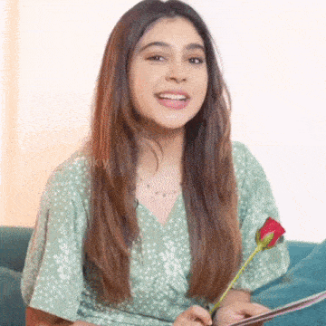 a woman in a green dress is sitting on a couch holding a rose .