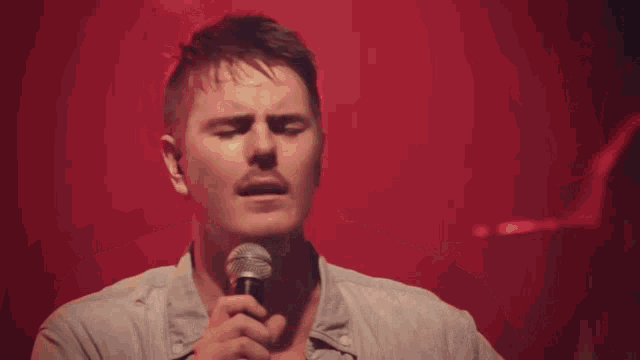 a man singing into a microphone in front of a red backdrop