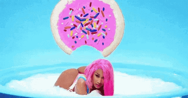 a woman with pink hair is laying in a pool of milk with a pink donut with sprinkles on it .