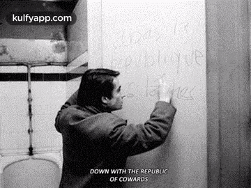 a man is writing on a wall in a bathroom with a toilet .