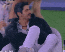 a man is sitting in a chair with his legs crossed and a woman is standing behind him .