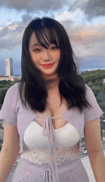 a woman wearing a purple top with a white lace top is standing in front of a cloudy sky