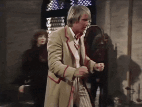 a man in a tan coat with red trim is standing in a dark room