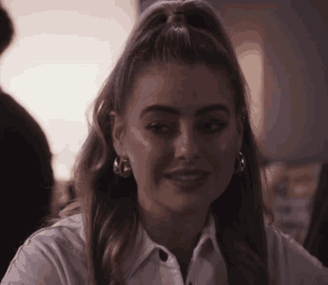 a woman with a ponytail and hoop earrings smiles