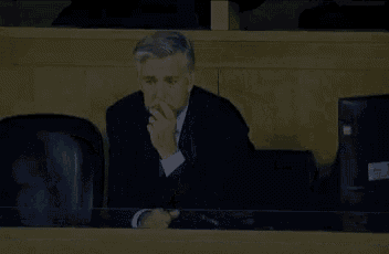 a man in a suit is sitting at a table with his hand on his face .