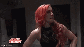 a woman with red hair is standing in a room with a sign that says wwe.com exclusive .