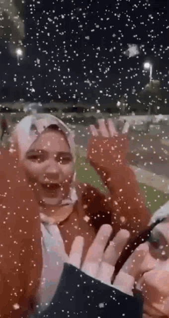 a woman in a hijab is waving her hands in the air while snow is falling around her