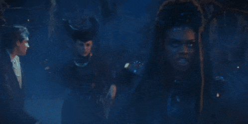 a group of people are standing in a dark room and one of them is wearing dreadlocks