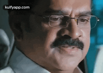 a man with a mustache and glasses is looking at the camera .