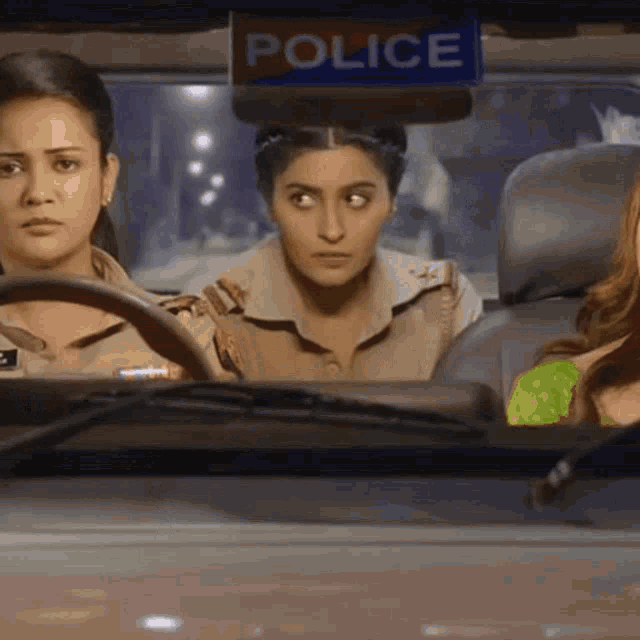 three women are sitting in a police car with a police sign above them
