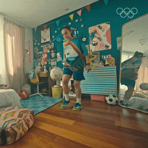 a girl is kicking a soccer ball in front of a wall with olympic rings