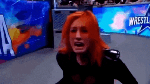 a woman with red hair is crying in front of a sign that says wrestle .
