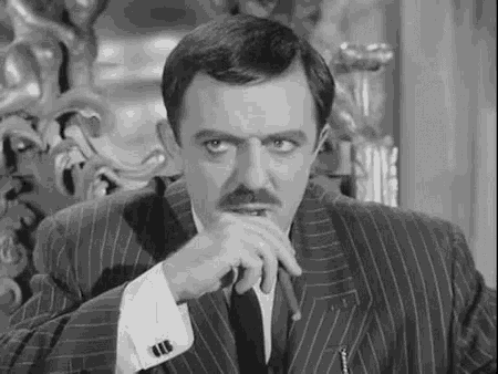 a man in a suit and tie is smoking a cigar and looking at the camera in a black and white photo .