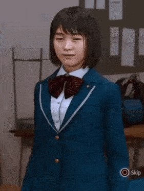 a girl in a blue school uniform is standing in a room with a skip button