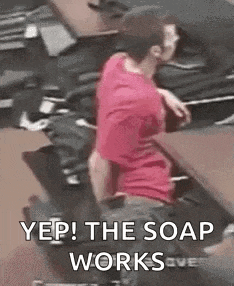 a man in a red shirt is sitting at a desk with his back to the camera and the soap works .