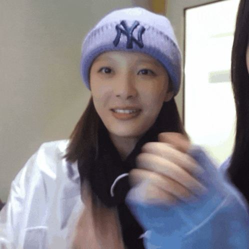 a woman wearing a purple ny hat smiles