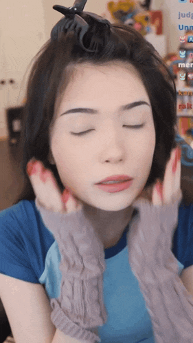 a woman with her eyes closed is wearing a blue shirt and grey gloves