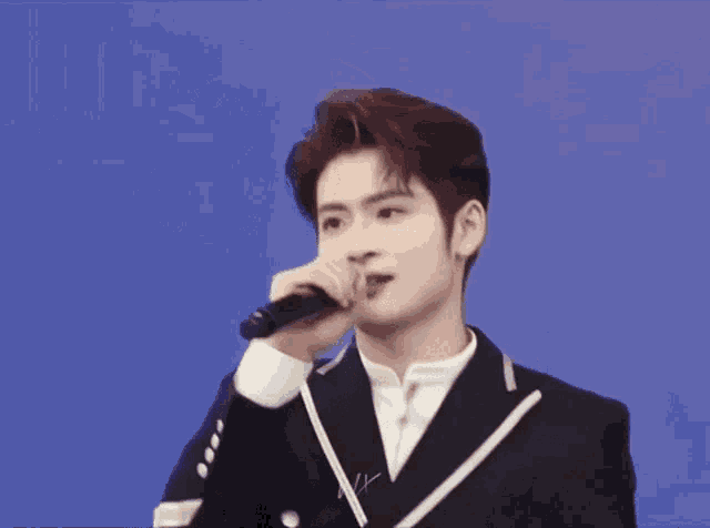 a man in a suit is singing into a microphone against a blue background