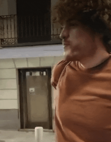 a man with curly hair is standing in front of a building and looking at something .