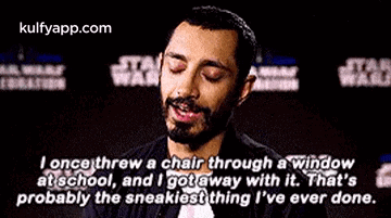 a man with a beard is sitting in front of a star wars sign and talking .