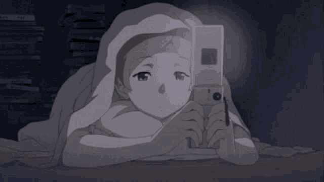 a girl is laying under a blanket looking at a cell phone