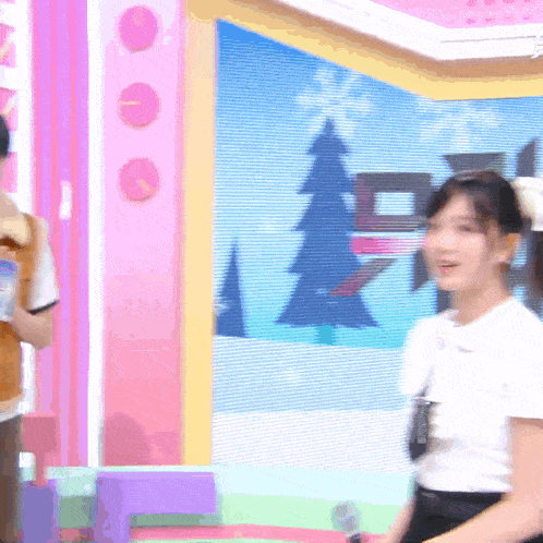 a woman in a white shirt stands in front of a pink wall with a christmas tree on it