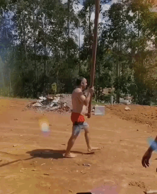 a shirtless man in red shorts is swinging a wooden pole