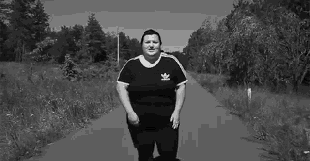 a black and white photo of a woman standing on a road in the woods .