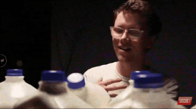 a man with glasses is surrounded by milk bottles with blue caps