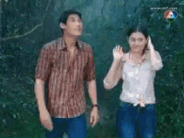 a man and a woman are standing next to each other in the woods and waving .