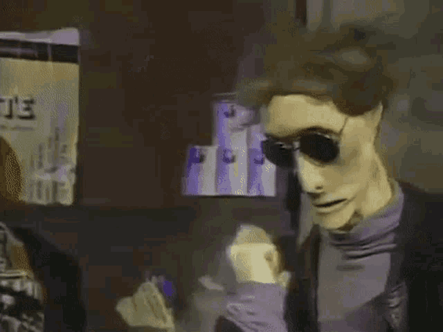 a puppet wearing sunglasses and a purple shirt is standing in front of a stack of cans .