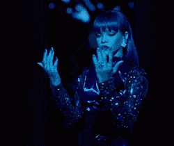 a woman with blue hair is standing in a dark room with her hands outstretched