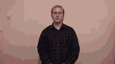a man in a plaid shirt is standing in front of a wall with his hands in his pockets .