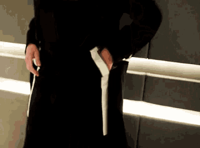 a man in a black coat and tie is holding a white object in his hand .