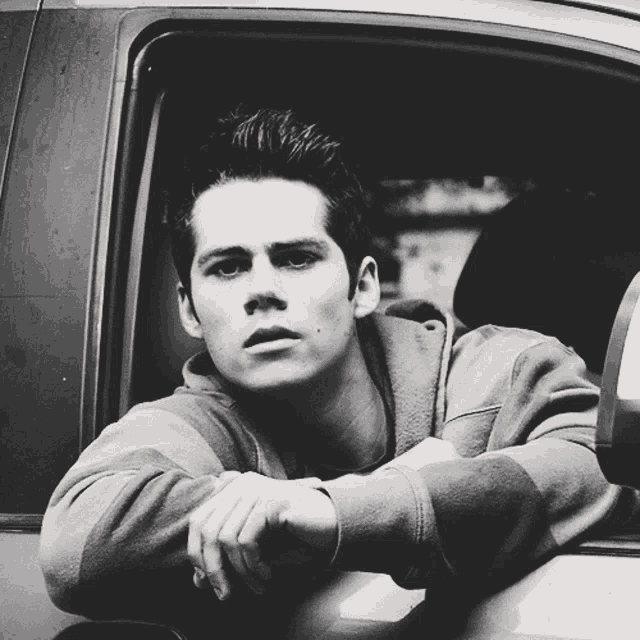 a black and white photo of a young man leaning on a car window
