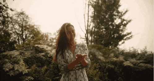 a woman in a white dress is standing in a field of trees