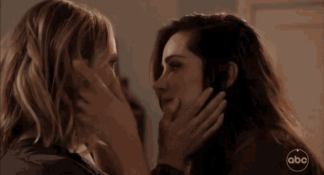 two women are kissing in front of a sign that says abc on it