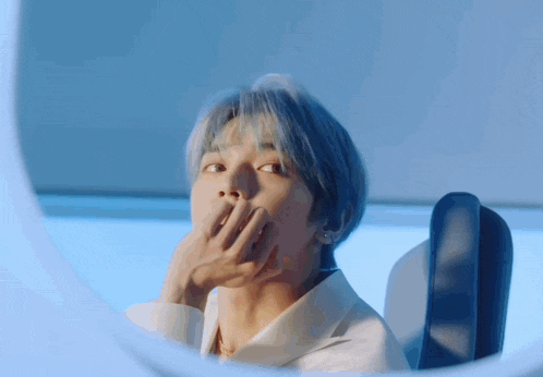 a man with blue hair covering his mouth with his hand