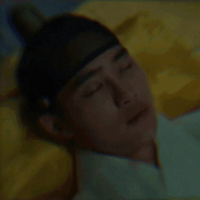 a man wearing a black hat is laying on a bed with a yellow pillow
