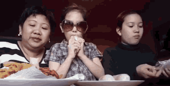 a girl wearing sunglasses is eating a sandwich while two other girls look on