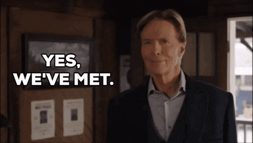 a man in a suit stands in front of a bulletin board that says yes we 've met
