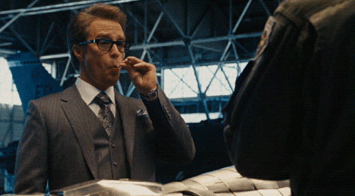 a man in a suit and tie is smoking a cigarette in a dark room