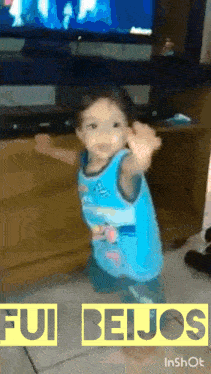a little boy in a blue shirt is dancing in front of a television with the words fui beijos in the bottom right corner