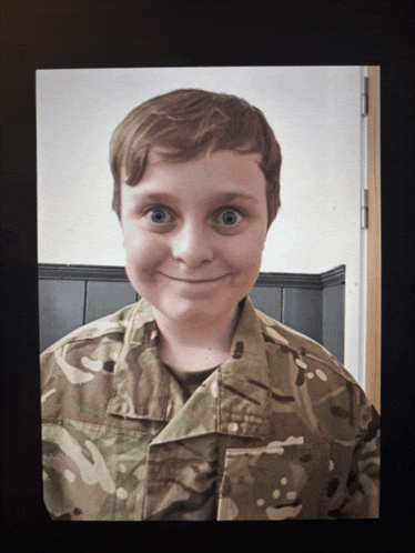 a young boy in a military uniform is smiling for the camera