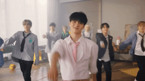 a group of young men are dancing in a room and one of them is wearing a pink tie