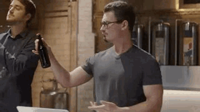 two men are standing next to each other in a kitchen holding bottles of wine .