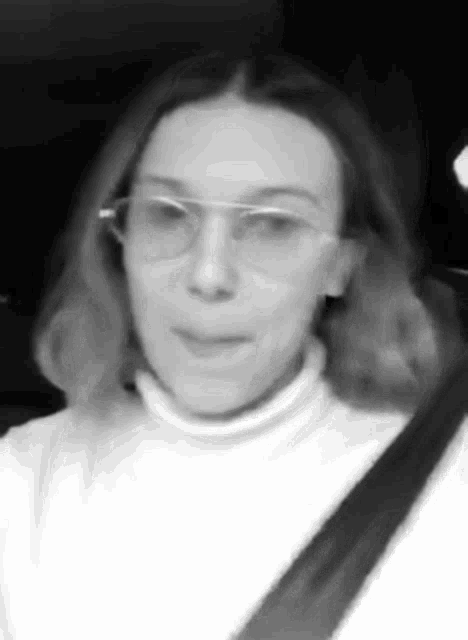 a black and white photo of a woman wearing glasses and a white sweater .