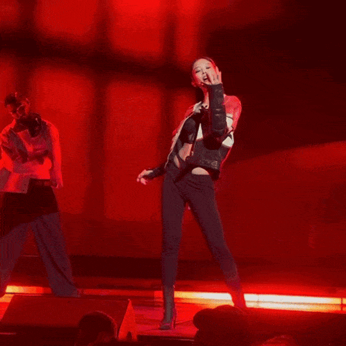a woman in a red jacket and black pants stands on a stage