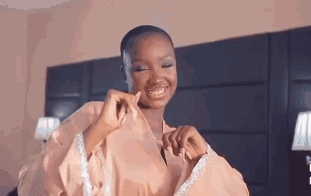 a woman is wearing a pink robe and smiling while standing on a bed .